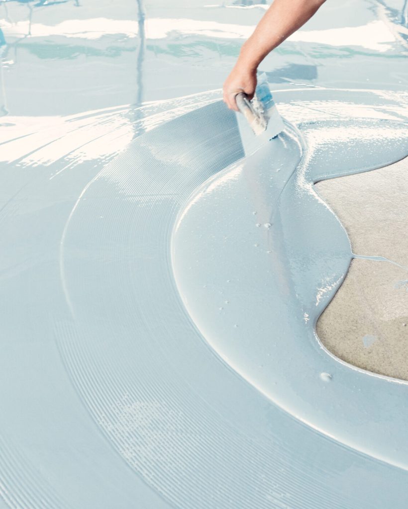 Construction worker spreading self-leveling concrete mixture over the floor using a trowel